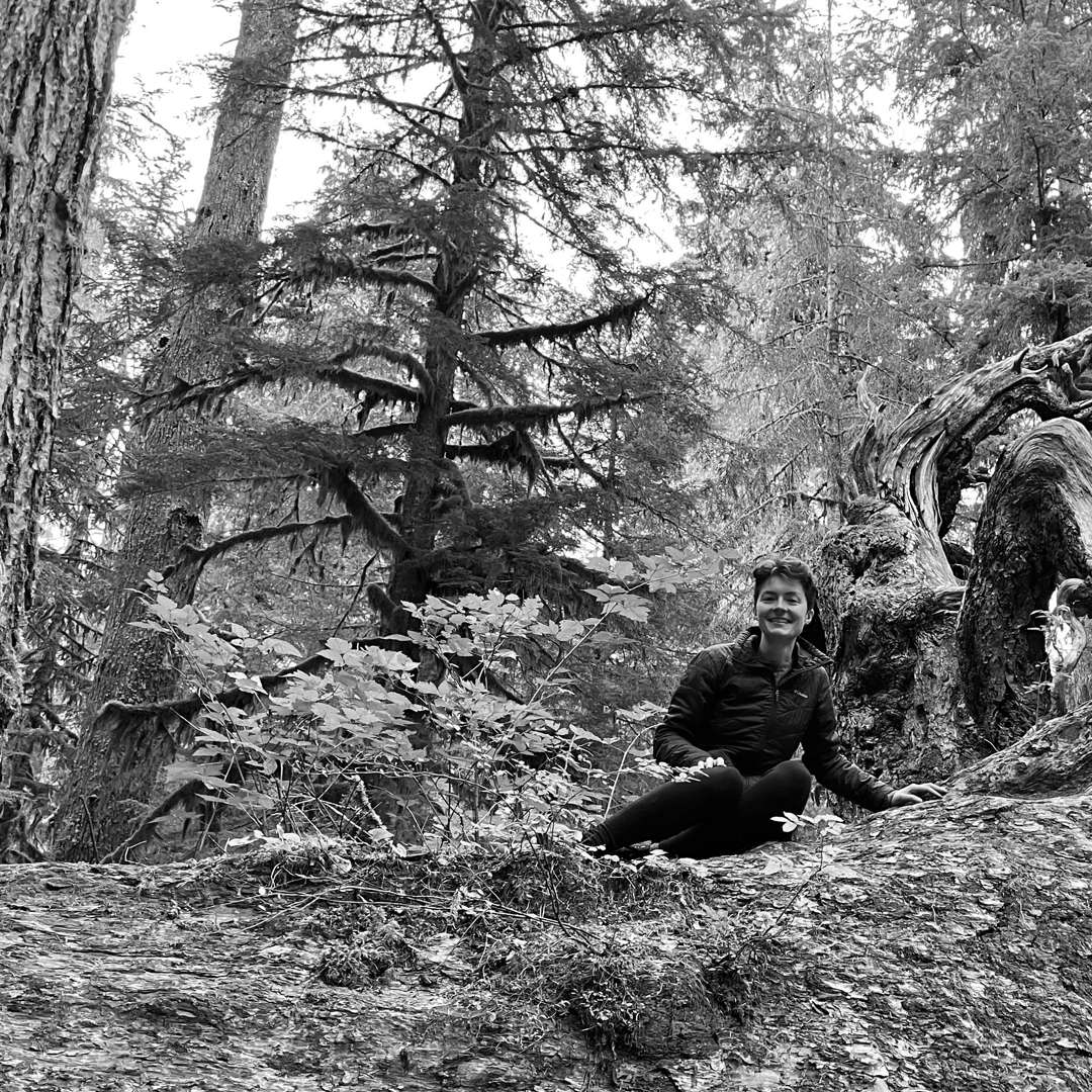 black and white of Calyn sitting on a massive fallen old growth log in the forest
